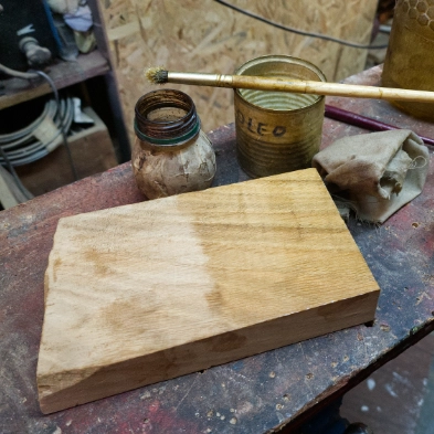 Oak block on the workbench beside a paintbrush, glass jar, and open tin of linseed oil