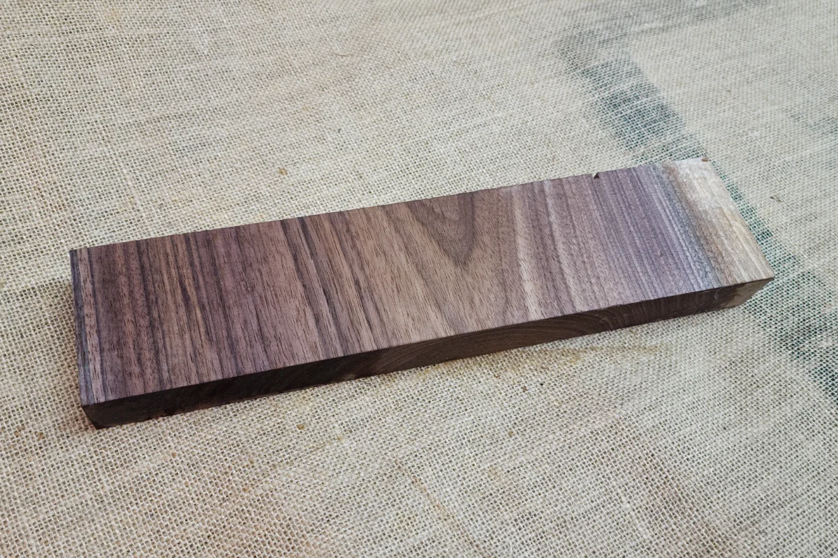 Smooth rectangular block of dark walnut with straight grain, resting on hessian