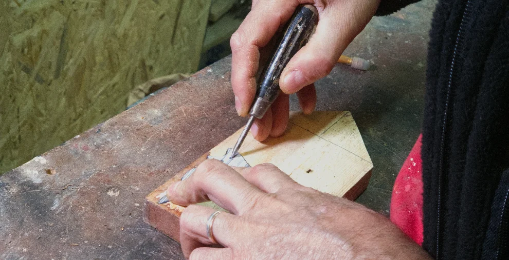 Close-up of hands pressing an awl into pencil-marked wood on the workbench